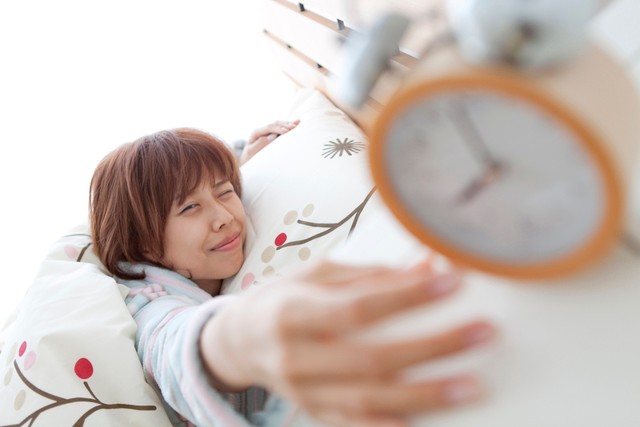 朝寝坊 目覚まし時計を止める女性