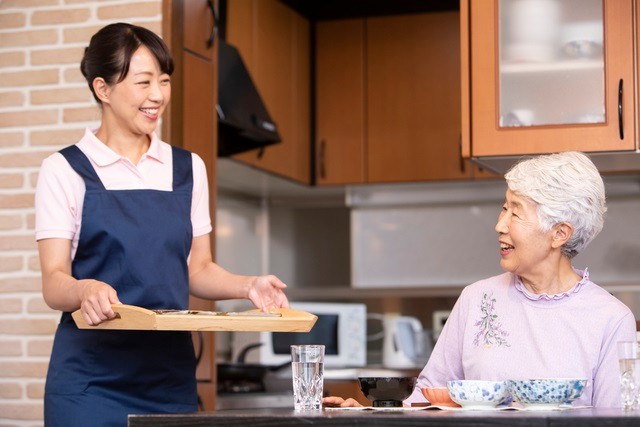 配膳をするヘルパーと喜ぶシニア女性