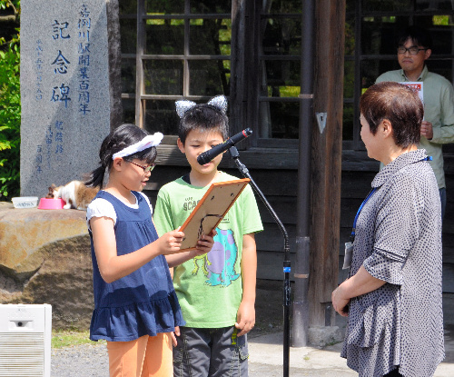 食事中のにゃん太郎(左奥)に代わり、任命証を受け取る山木委員長(右)=鹿児島県霧島市隼人町嘉例川