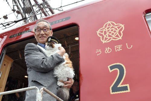 ニタマを抱いて「うめ星電車」に乗り込む小嶋光信・和歌山電鉄社長=和歌山市伊太祈曽
