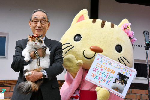 小嶋光信社長に抱かれたニタマ駅長と滋賀県湖南市のPRキャラクター「こにゃん」