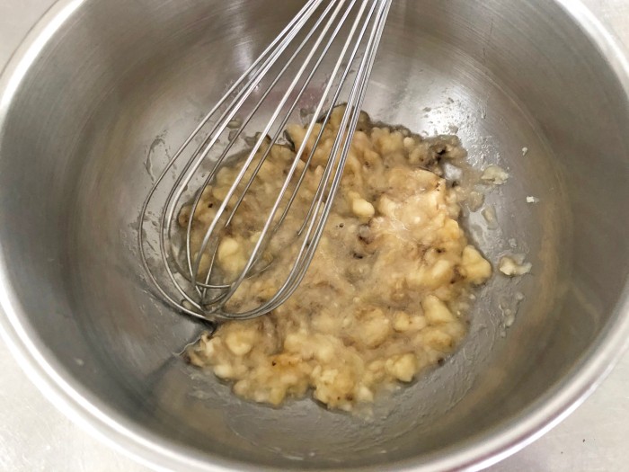 （a）薄力粉とベーキングパウダーを合わせてふるいにかける。マフィン型にグラシンカップを敷く（紙のマフィン型でも可）。ボウルにバナナを入れ、泡立て器でつぶす。