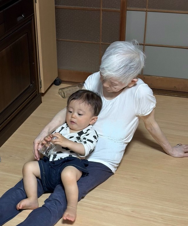 ひいおばあちゃんの膝の上でくつろぐ曾孫。安心しきった表情で手元のおもちゃに夢中／Kei’s mommyさん（@instaofkeismom）提供