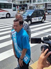 参院選の第一声に飛び入り参加した松尾貴史（背後）に駆け寄るラサール石井＝ＪＲ新宿駅前