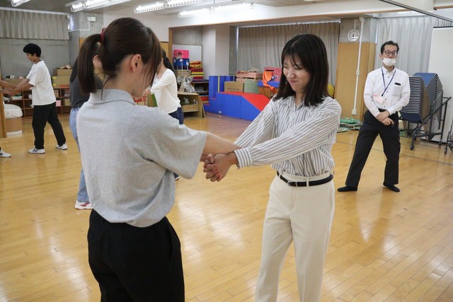 腕をつかまれ、両手を組んで振りほどこうとする記者（手前右）