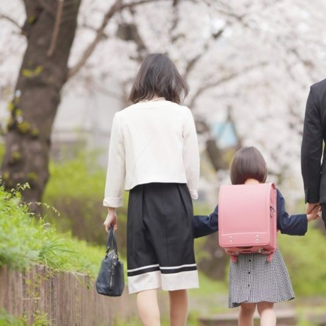 桜の下、手をつないで歩く親子