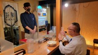 西麻布のラーメン店「楽観」のカウンターで國元店長（左）に事情聴取する小川泰平氏