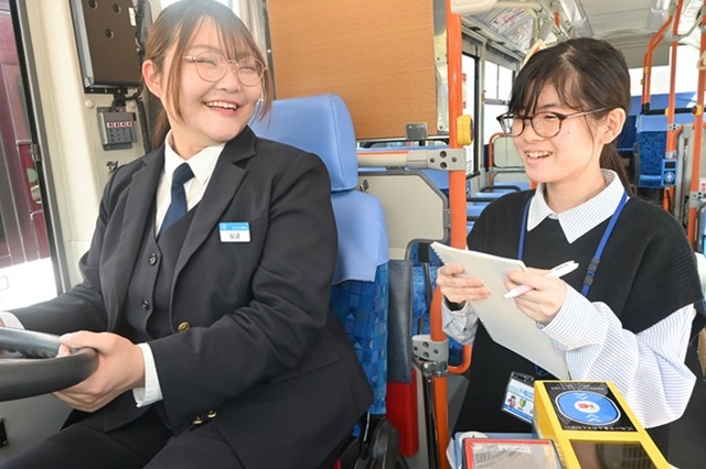 先輩の運転手から乗客の対応について学ぶ山本夏楓さん（右）＝島根県松江市、市交通局