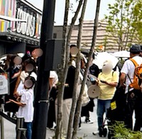 万博会場では、パビリオンに並んだり休憩や食事のため、「アウトドア用の折りたたみ椅子」は必須アイテムだった。画面中央には円盤状に畳んだ通称「万博椅子」を持った人の姿も（画像：筆者撮影）