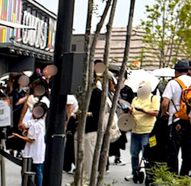 万博会場では、パビリオンに並んだり休憩や食事のため、「アウトドア用の折りたたみ椅子」は必須アイテムだった。画面中央には円盤状に畳んだ通称「万博椅子」を持った人の姿も（画像：筆者撮影）