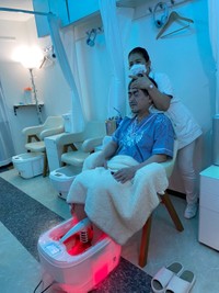 鼻の穴に挿入したチューブから水素を吸入しながら、解毒機器の湯に両足を入れ、楊珍雲院長（後方）の施術を受ける＝東京・新橋の珍雲堂本店