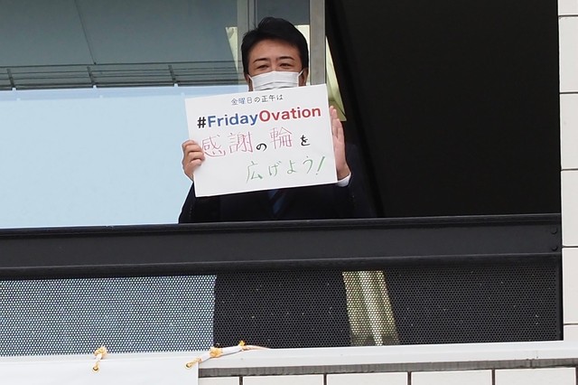 「感謝の輪を広げよう！」と書いたメッセージボードを掲げる高島市長