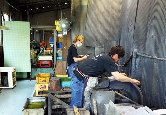 包丁を研ぐ増谷さん（右）。研ぐ姿勢は、腰や全身に大きな負担がかかる＝林敏行撮影