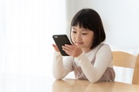 スマホを手にする小学生の女の子 ※画像はイメージです（taka/stock.adobe.com）