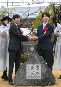 記念碑を前に、笑顔で手を取り合う藤井聡太さん（右）と武豊さん＝京都市伏見区・京都競馬場　