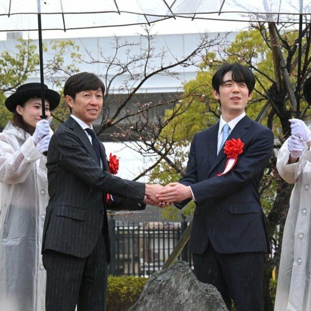 記念碑を前に、笑顔で手を取り合う藤井聡太さん（右）と武豊さん＝京都市伏見区・京都競馬場　