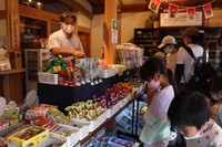 日本酒の試飲スペースを駄菓子販売コーナーに切り替えた「酒商　おまっとう」の店内。「リピーターの子どもいる」と話す小松さん（左）＝京都市右京区嵯峨釈迦堂
