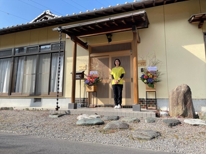 新居浜市の自宅前で。nobitaの看板もかかる。畑を耕し、すっかり田舎暮らしを楽しんでいる（富永さん提供）