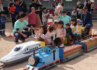手作りのミニ列車で子どもたちを楽しませる奥村さん（右端）。後方から見守る＝２０１８年、亀岡市内