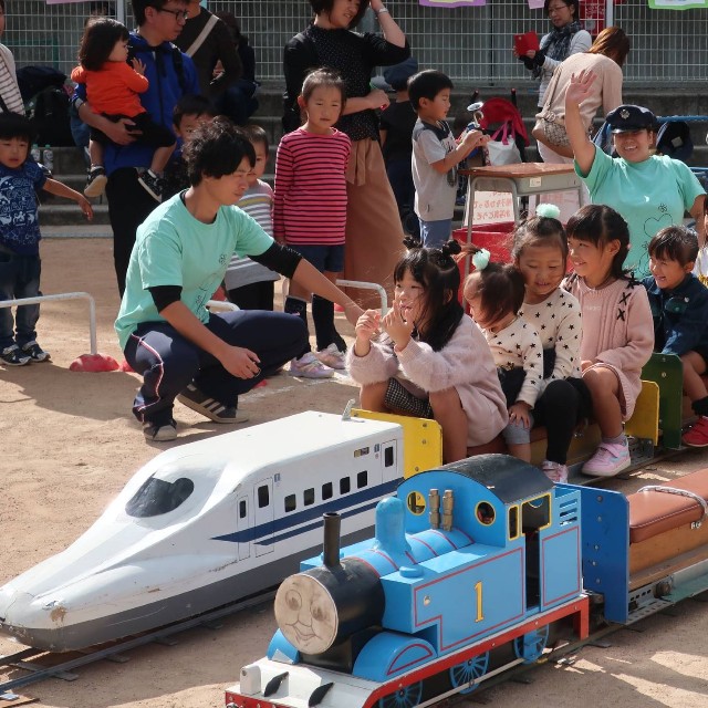 手作りのミニ列車で子どもたちを楽しませる奥村さん（右端）。後方から見守る＝２０１８年、亀岡市内