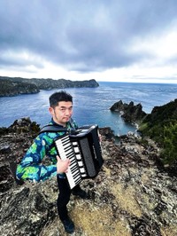 小笠原諸島の父島でアコーディオンを奏でるミュージシャンの田ノ岡三郎。朗読劇には演奏で参加する