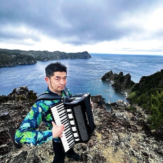 小笠原諸島の父島でアコーディオンを奏でるミュージシャンの田ノ岡三郎。朗読劇には演奏で参加する