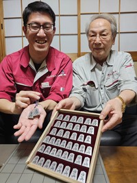 桐箱に収納したアルミ製の駒を披露する金森さん（右）とアルミ駒のストラップを手にする紀本さん＝宇治市槙島町・金森製作所

