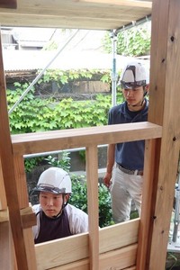 棟梁の田中さん（右）の指導の下、化粧板を張り付ける作業をする片山さん