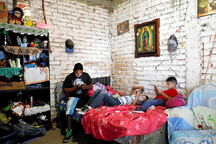 Arturo, 33, a Mexican migrant, who was denied a visa to the United States, looks at his mobile phone next to his sons Juan, 10 and Javen, 6, inside their house in Neutla, Guanajuato state, Mexico, April 9, 2019. Picture taken April 9, 2019. REUTERS/Edgard Garrido