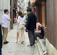 店舗街にある住宅の前に座り込み、道を塞いで撮影をしている訪日外国人観光客（画像：筆者撮影　※顔部分に加工をしています）