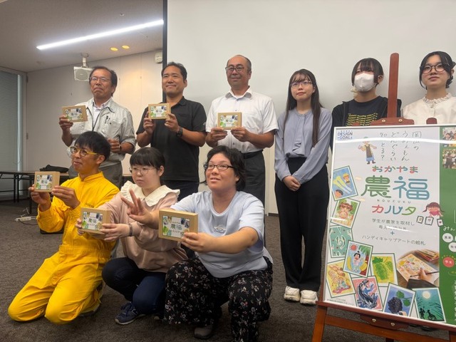 カルタの完成を喜ぶアーティストや、制作に協力した農畜水産業者ら＝岡山市北区駅元町