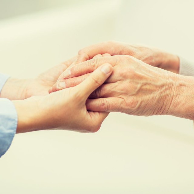 高齢の人の手をやさしく握る介助者の手※画像はイメージです （Syda Productions/stock.adobe.com）