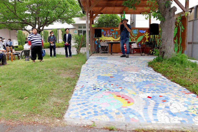 障害者施設の利用者や住民がタイルで制作した小道。芸術家の井上信太さん（右奥）がセレモニーで紹介した＝亀岡市大井町