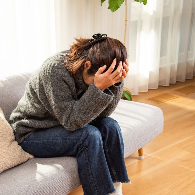 リビングルームで頭を抱えるうつ病の女性※画像はイメージです（years/stock.adobe.com）
