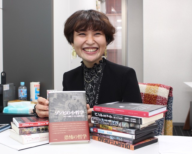 福田安佐子助教が手に持っているのは、自身が翻訳を担当した「ゾンビの小哲学」（マキシム・クロンブ、人文書院）。「増刷がかからないと印税が入りません！（笑）」＝国際ファッション専門職大学