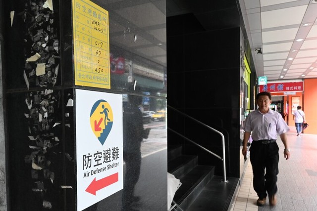 台北市の商業ビル１階に貼られた、地下防空壕の位置を示す新旧の標識。上の黄色いものが旧版で、収容可能人数が記されている＝石田耕一郎