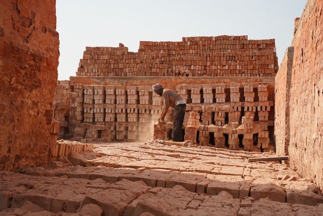 旧式のれんが工場で、赤茶色の粉じんが舞う中、男性が焼き上がったれんがを取り出していた=2024年5月3日、ダッカ郊外、荒ちひろ撮影