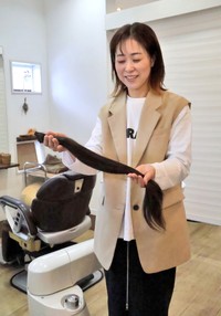 女子中学生が寄付した約６０センチの髪を手にする美容師の横村さん（八幡市美濃山・カルム）
