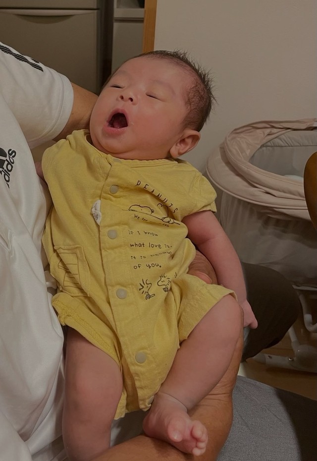 1枚目。義父に抱っこされ、あくびをする赤ちゃん（まるさん提供）