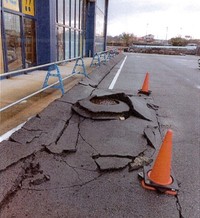 店の下の地盤と一緒に下がった駐車場。マンホールが残り、店舗と同様に浮き上がって見える状態に　※発災直後（提供：株式会社ロッキー）