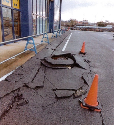 店の下の地盤と一緒に下がった駐車場。マンホールが残り、店舗と同様に浮き上がって見える状態に　※発災直後（提供：株式会社ロッキー）