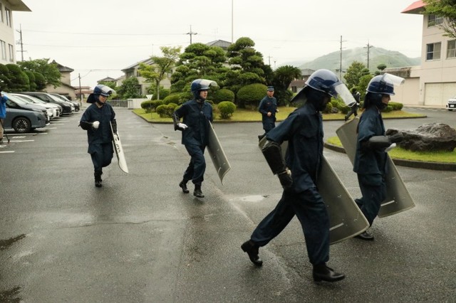 警備実習で盾を持って走る記者（左端）。徐々に隊列から遅れていく