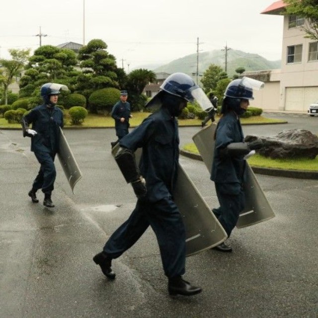 警備実習で盾を持って走る記者（左端）。徐々に隊列から遅れていく
