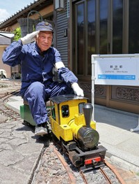 自宅に敷設したレールでミニ蒸気機関車に乗る奥村さん。北陸新幹線の「新京都駅」の駅名標を作ってみたという（亀岡市篠町）