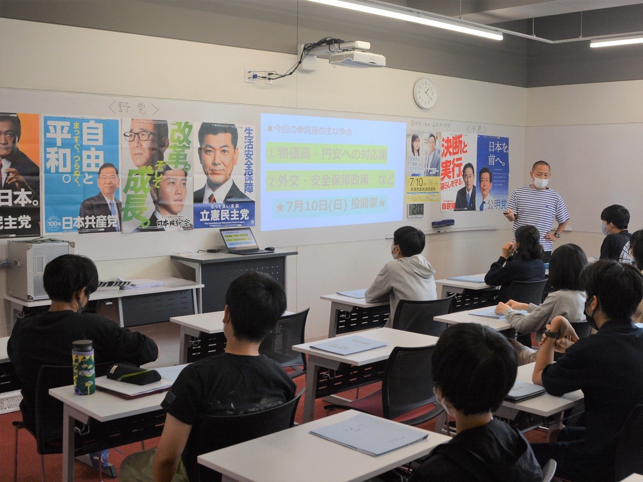 政党ポスターの前で語る大畑方人先生