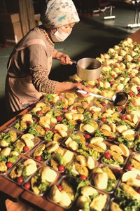 宮城県気仙沼市の松岩公民館避難所で野菜や果物の入ったパックにドレッシングをかける現地の女性。「地元のおかあさん」たちも被災者を支えた