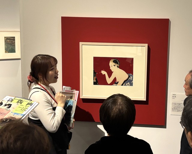 学芸員の説明に聞き入る来場者たち。新版画の奥行きが静かに広がる＝神戸ファッション美術館