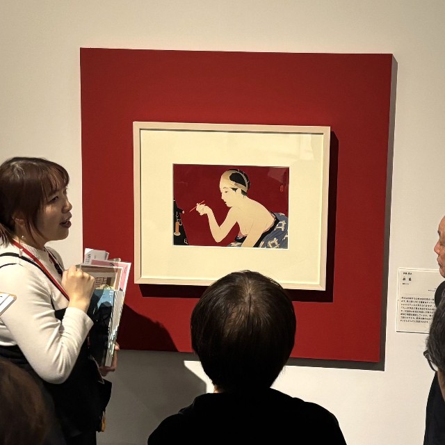 学芸員の説明に聞き入る来場者たち。新版画の奥行きが静かに広がる＝神戸ファッション美術館