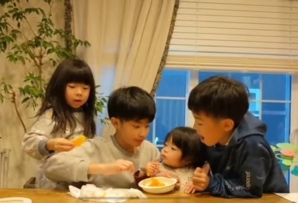 末っ子ひなちゃんにみかんを食べさせてあげる兄姉（提供：	＠pesanfamilyさん）