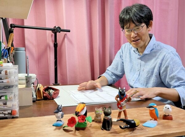 自宅の作業スペースで、作品を前に笑顔を見せる米井さん（亀岡市大井町）